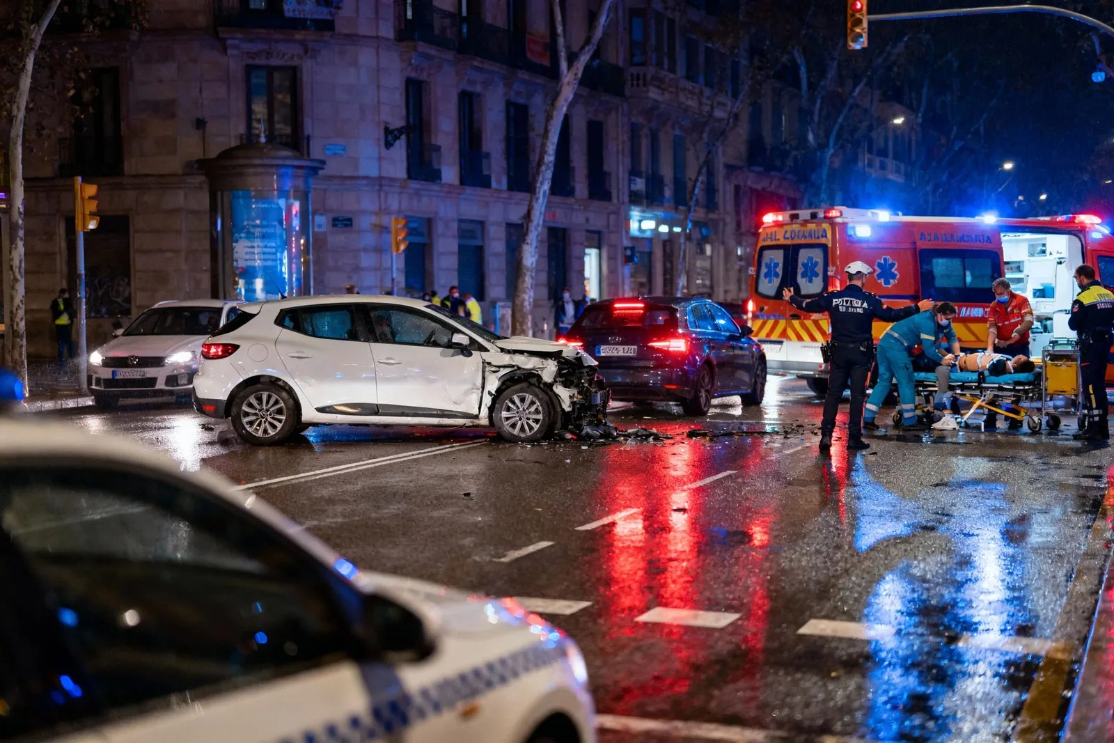 Accident de trànsit nocturn en un carrer de Barcelona, amb els serveis d'emergència treballant sota la pluja